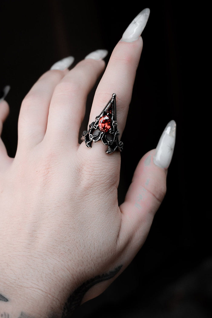 Hand wearing a decorative ring with a red gemstone against a dark background