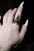 Hand wearing a decorative ring with a red gemstone against a dark background
