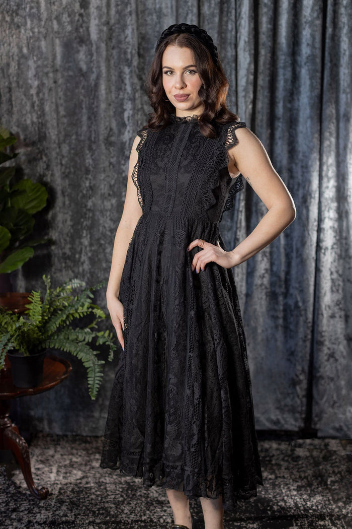 Woman wearing a black lace dress against a textured gray curtain background