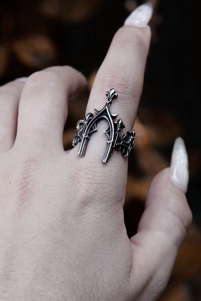 Silver ring with intricate design on a finger against a blurred background