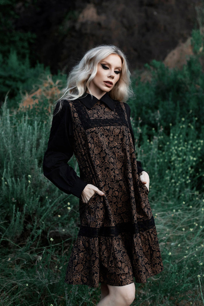 Woman in a black and brown patterned dress standing in a forest setting