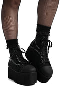 Black platform boots with chain details worn with fishnet stockings on a white background