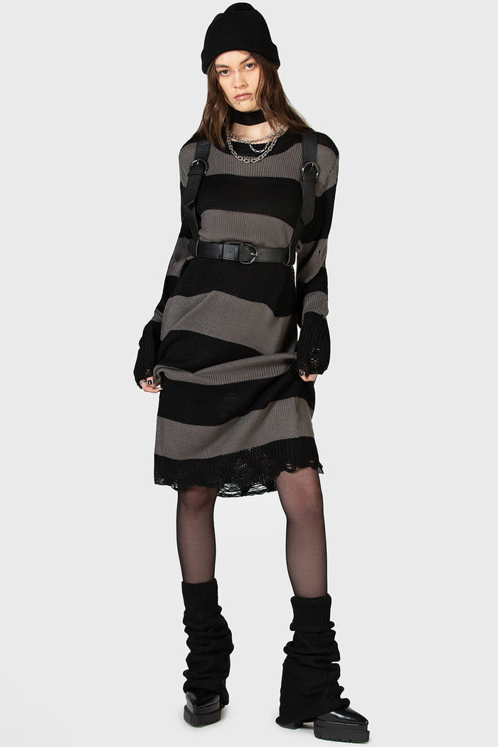 goth girl wearing a black and grunge gray striped dress with a high-waisted punk belted harness, black boots, and a black beanie on a white background.
