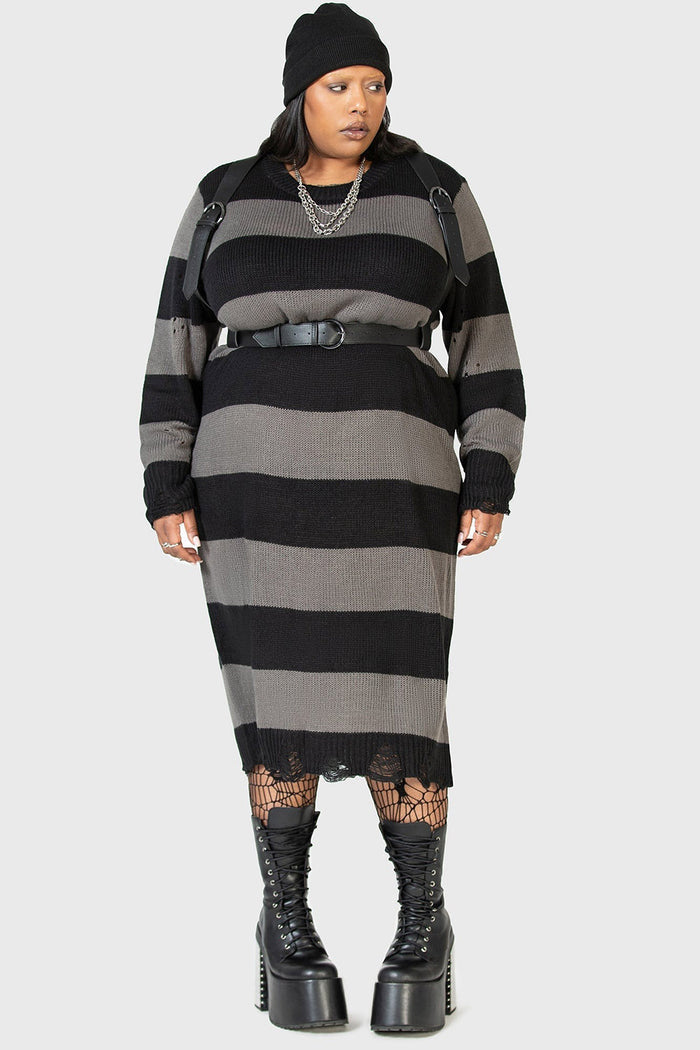 goth girl wearing a black and gray striped emo dress with a high-waisted plus size gothic belted harness and platform boots on a white background