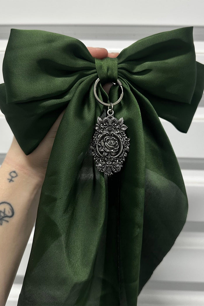 Green bow with a decorative silver rose charm against a neutral background