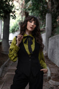 Woman in a green blouse and black vest standing outdoors with trees in the background