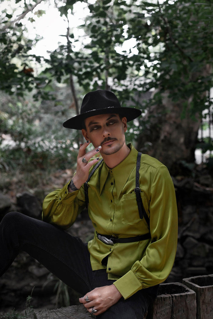 Man in a green shirt and black hat sitting outdoors with trees in the background