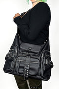 Person wearing a large black leather bag with multiple pockets and straps on a white background