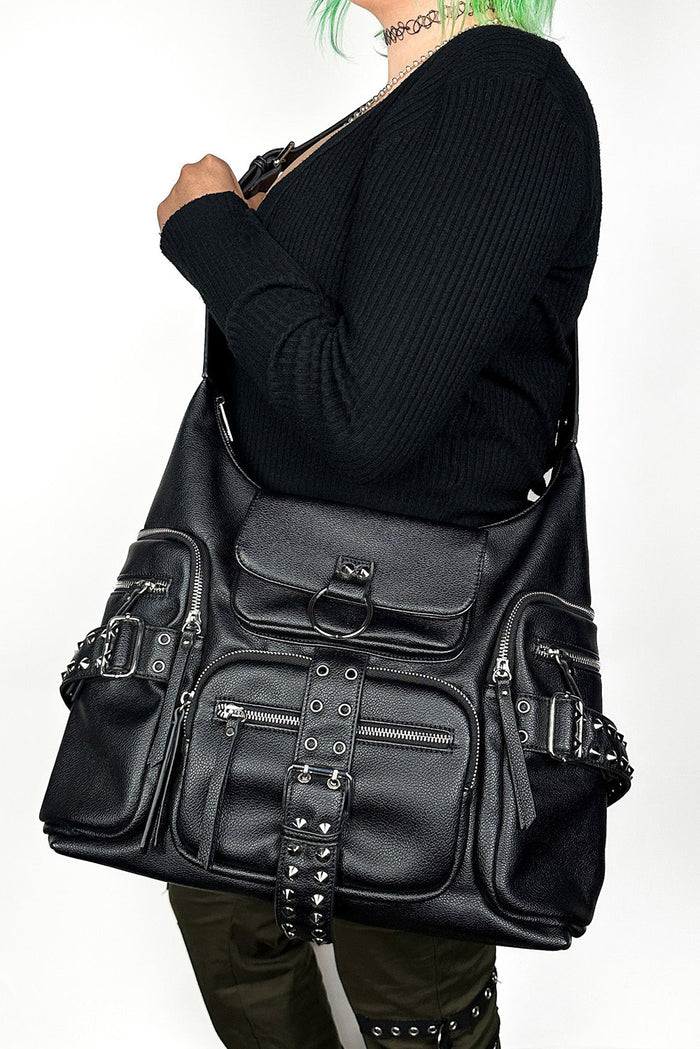 Person wearing a large black leather bag with multiple pockets and straps on a white background