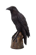 Black crow figurine on a wooden perch against a white background