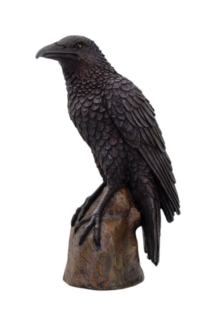 Black crow figurine on a wooden perch against a white background