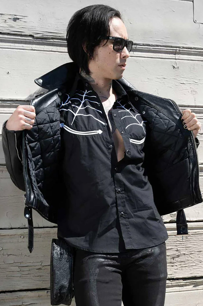 Person wearing a black jacket with an spiderweb shirt against a wooden background