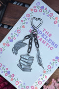 Keychain with books and feathers on a card with floral designs and text.