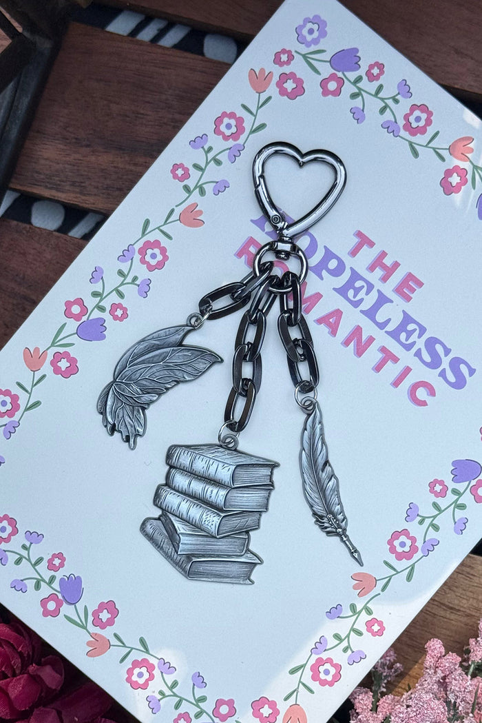 Keychain with books and feathers on a card with floral designs and text.