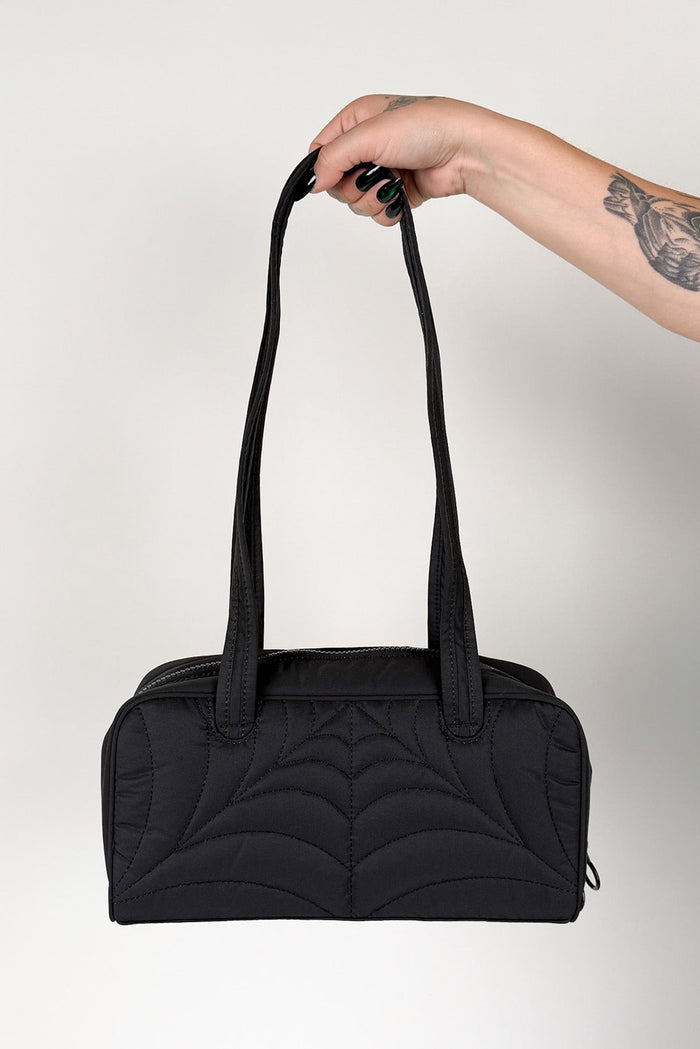 Black quilted handbag held by a hand with a tattoo on a light gray background