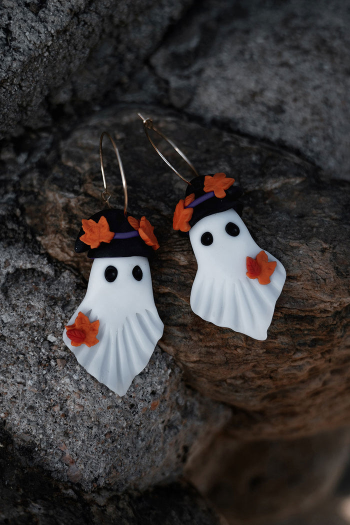 Halloween-themed ghost earrings with orange leaves on a stone surface